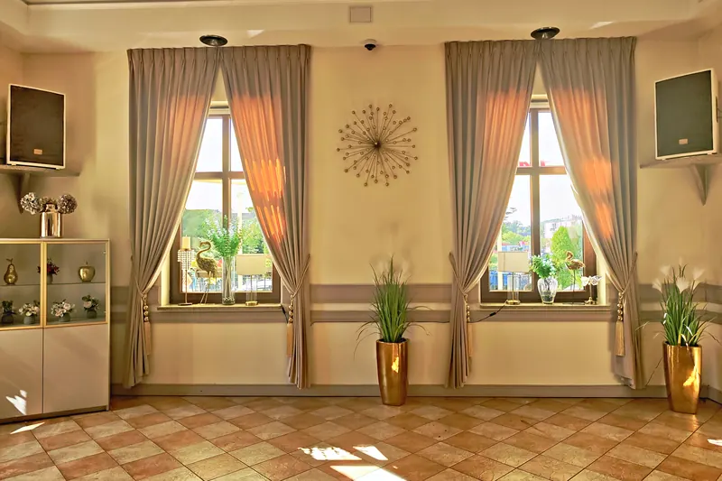Sala weselna hotelu Kamienica w Sulęcinie: dwa okna z beżowymi zasłonami podpiętymi złotymi chwostami