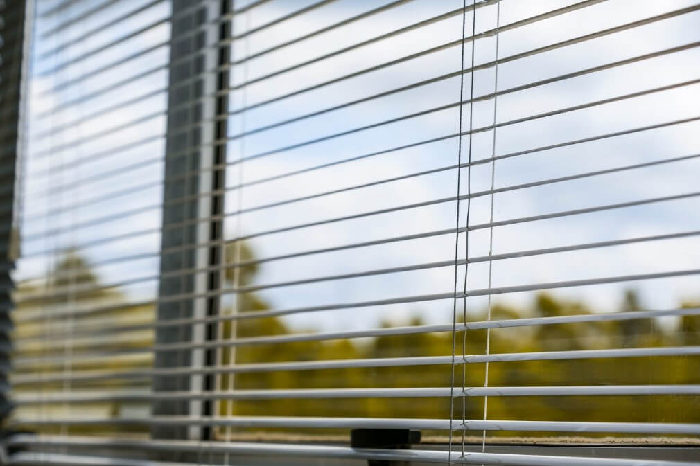 Żaluzje poziome na oknie z widokiem na zewnątrz, regulowane lamele kontrolujące światło dzienne we wnętrzu nowoczesnego pomieszczenia